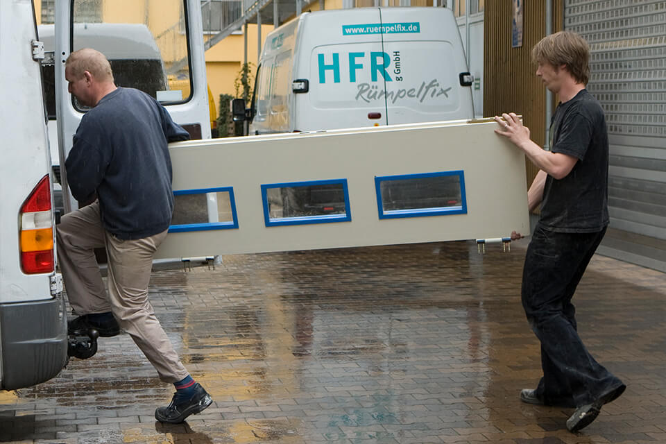 Zwei Männer tragen eine Tür. Hinter Ihnen steht ein HFR Möbeltransporter.