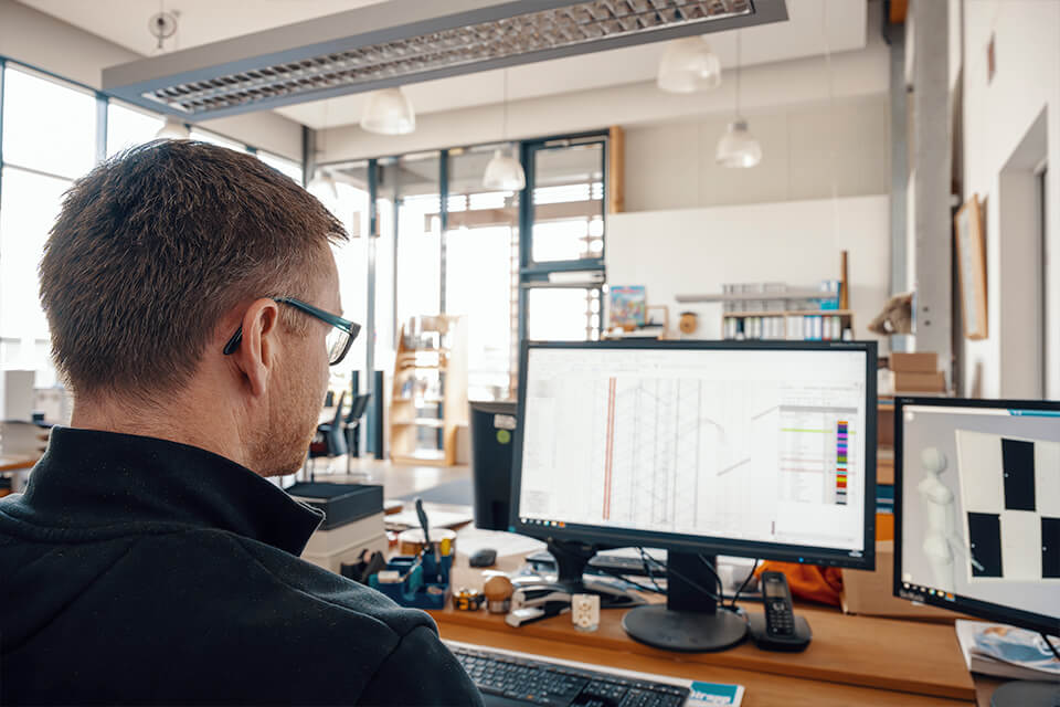 Mitarbeiter sitzt vor Computer mit Designprogramm.