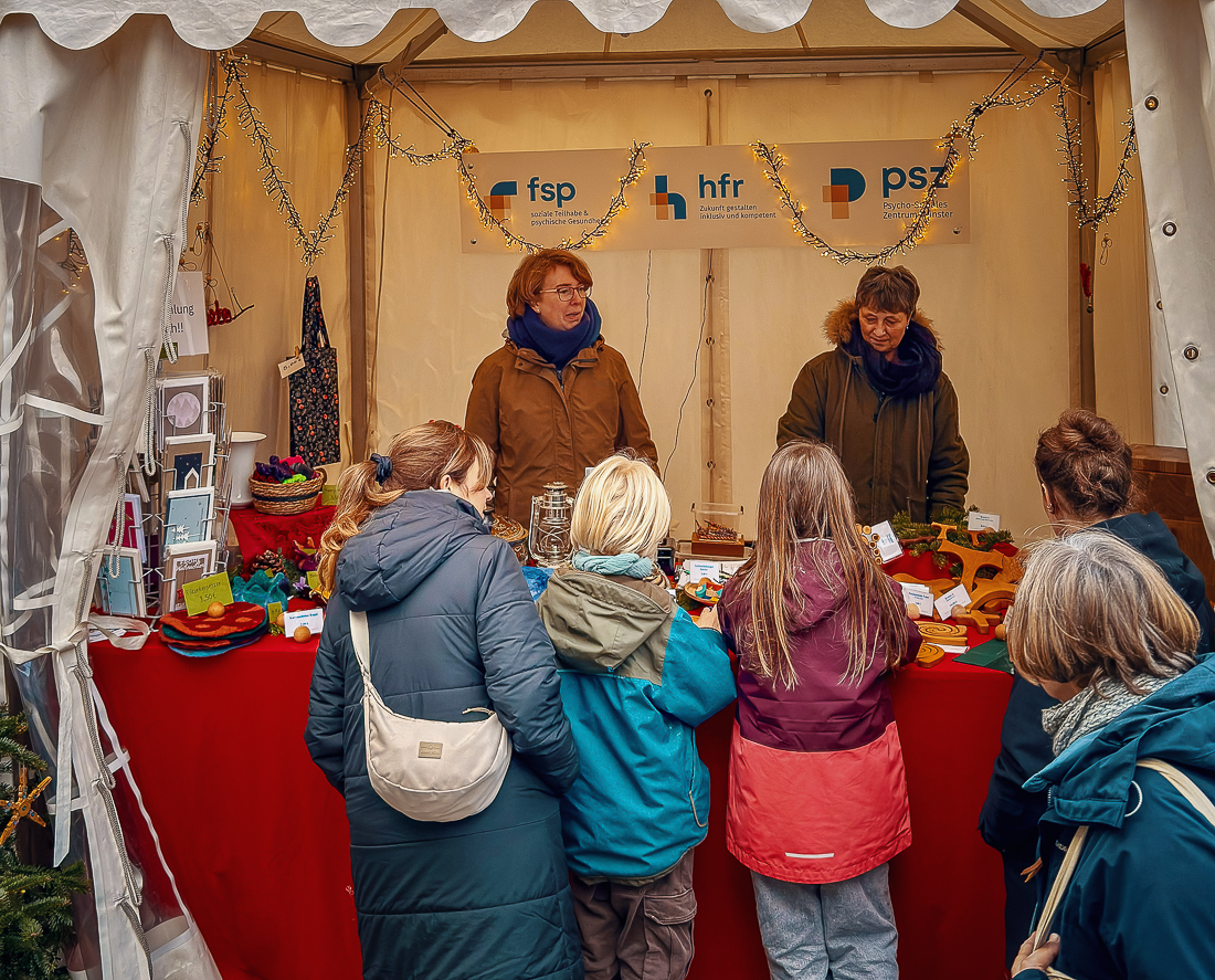 Handgemachte Produkte und Dekoartikel am HFR-Weihnachtsmarktstand mit Besucherinnen.